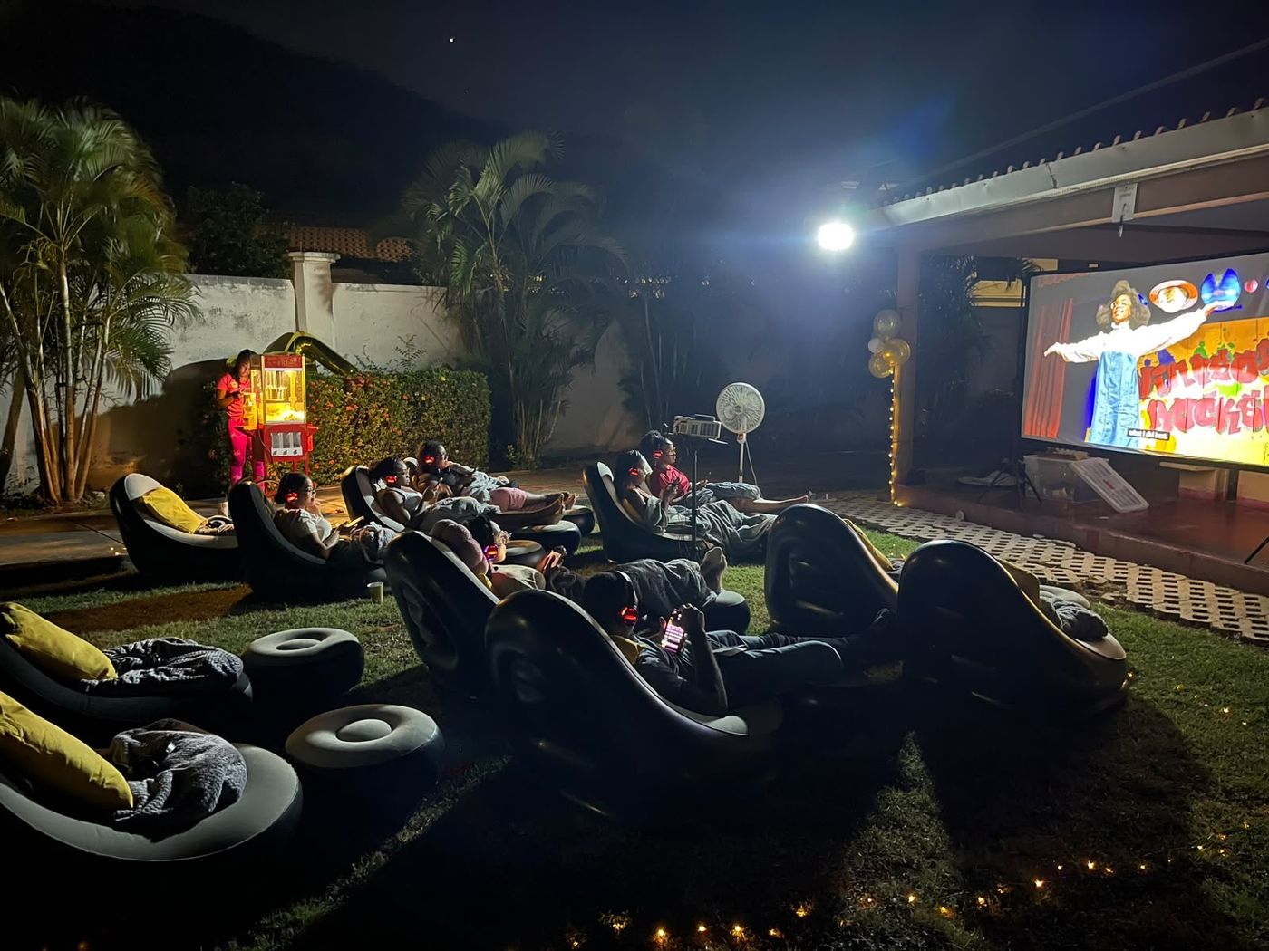 Guests watching a film at a back yard outdoor cinema in Jamaica at night